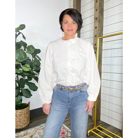 Woman wearing a white blouse and blue jeans standing in a room with a plant and a yellow rack.