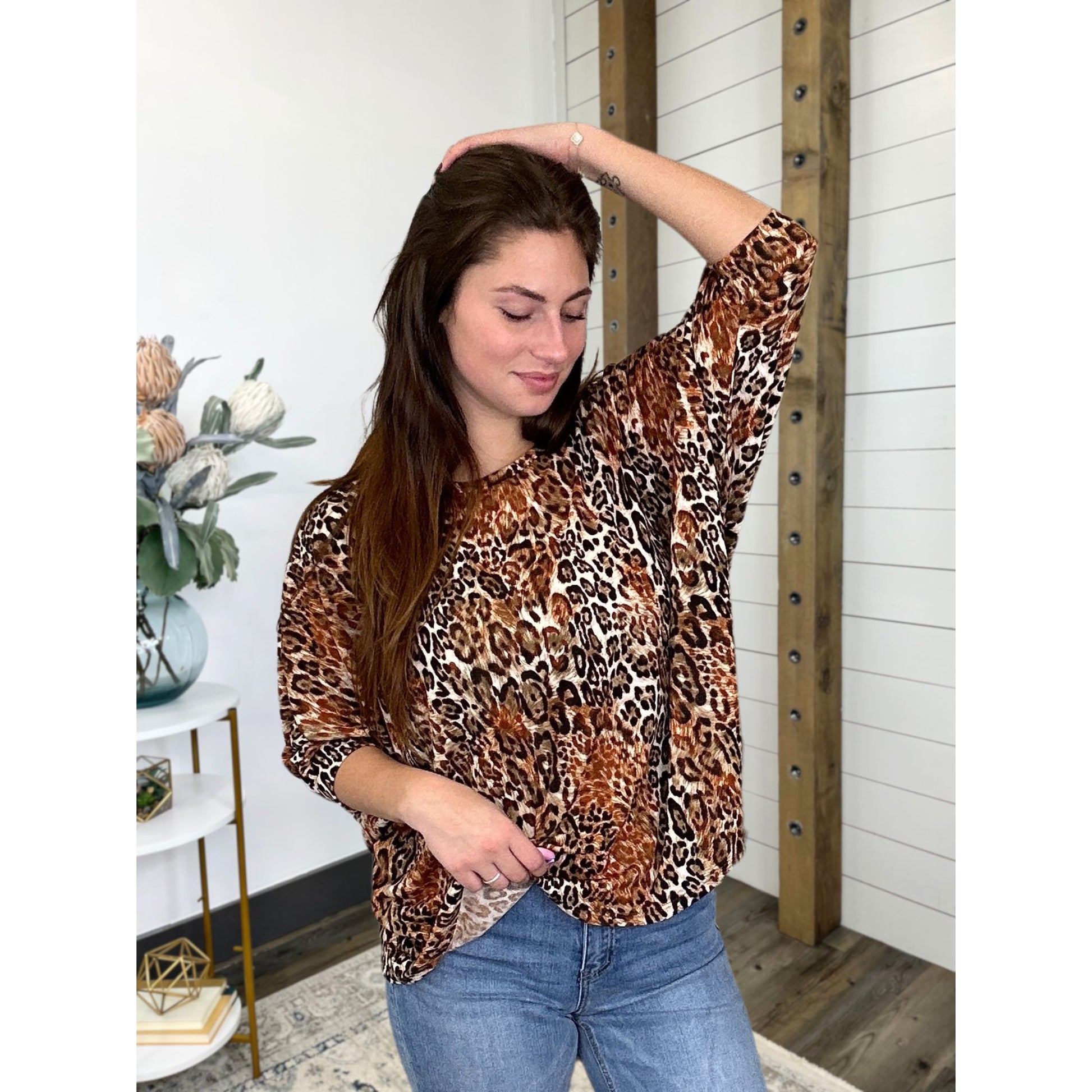A woman wearing a leopard print top with 3/4 dolman sleeves and round neckline, in a casual setting.