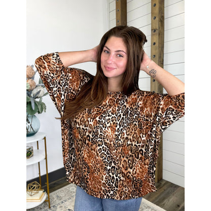 A woman wearing a leopard print, 3/4 dolman sleeve, round neck top.
