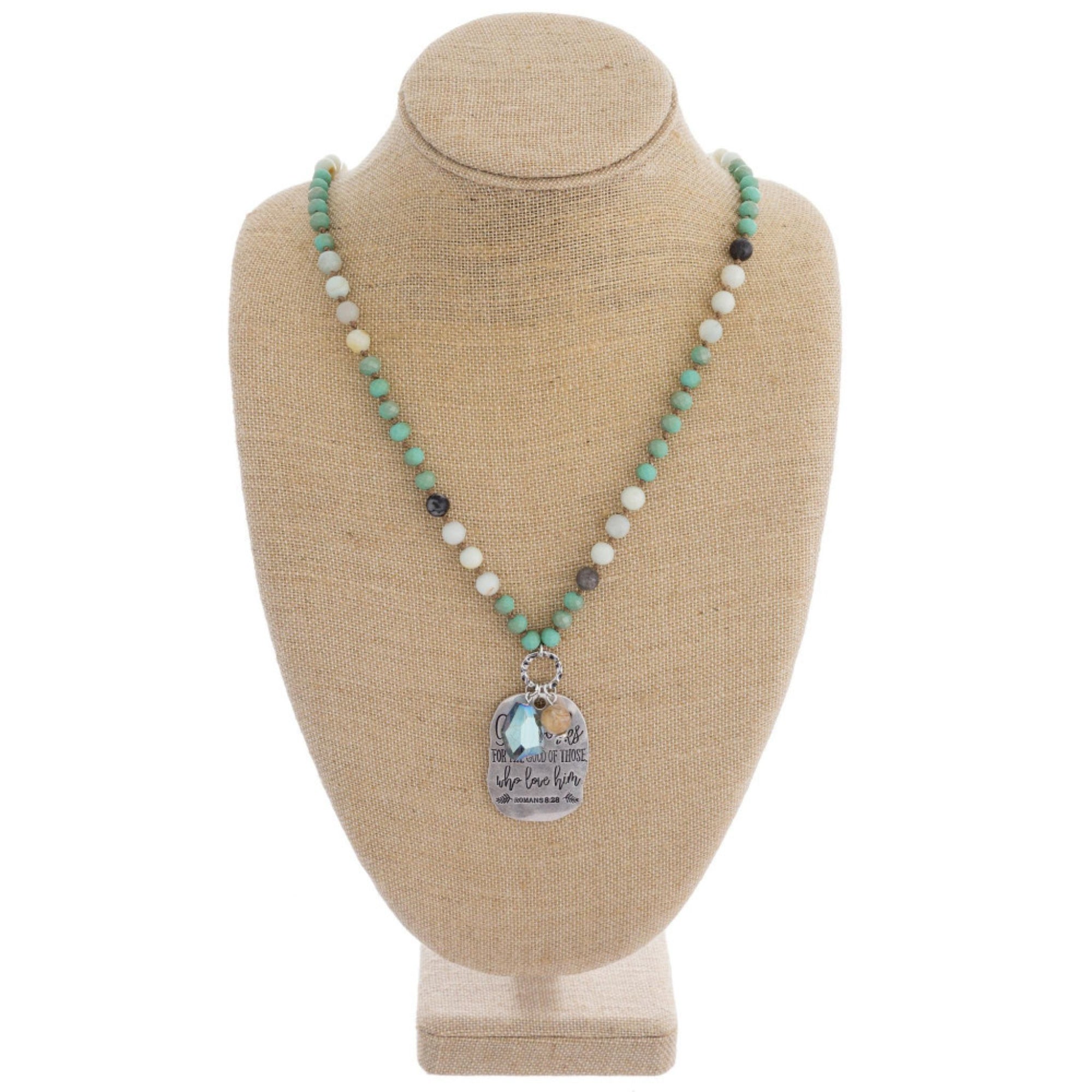 Long beaded necklace with engraved message, "God works for the good of those who love him. Romans 8:28."
