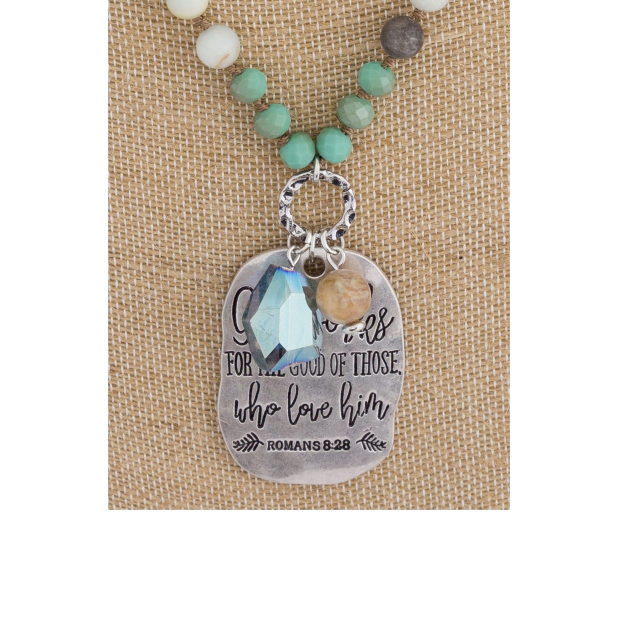 Long beaded necklace with engraved message, "God works for the good of those who love him. Romans 8:28."