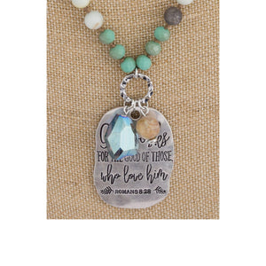 Long beaded necklace with engraved message, "God works for the good of those who love him. Romans 8:28."