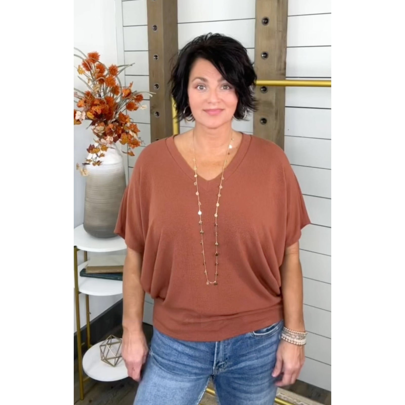 Woman wearing a brown top and blue jeans standing in a room with decorative elements.
